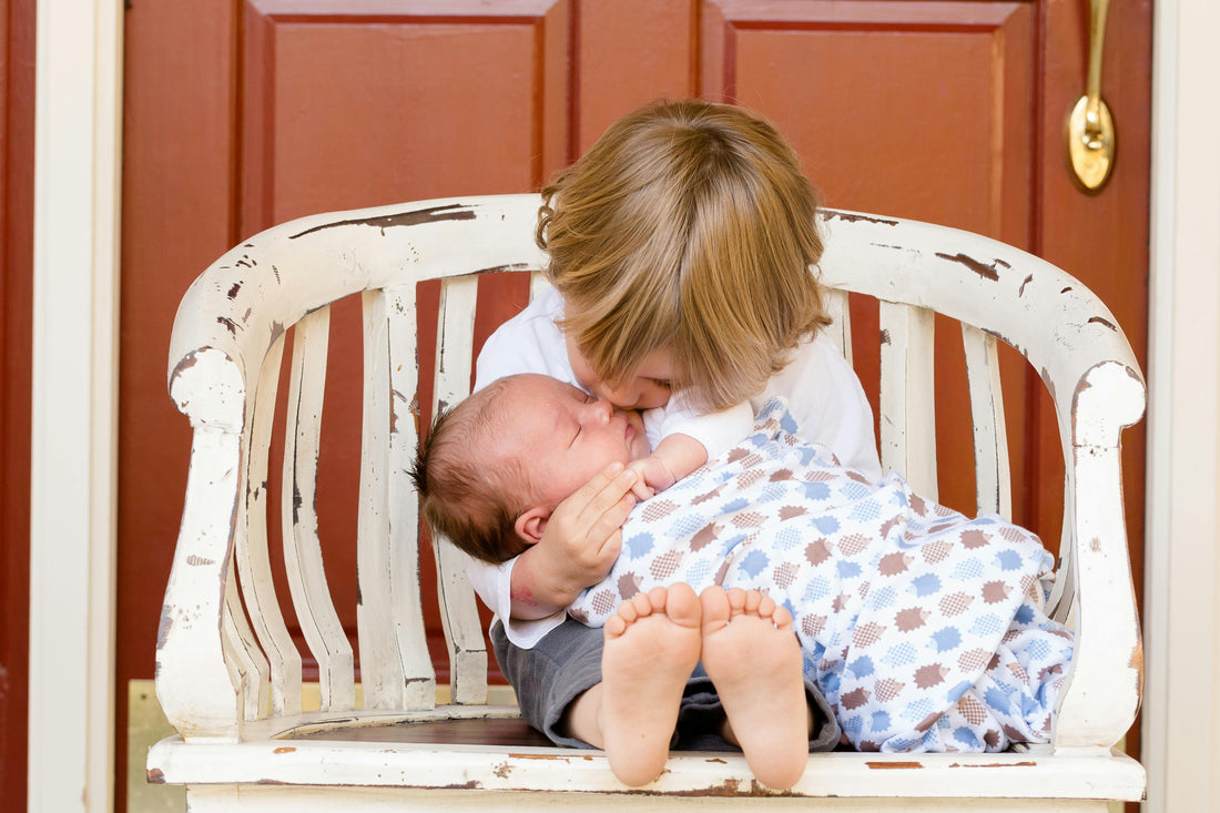 Toddler boy holds younger baby sibling in his lap on a bench