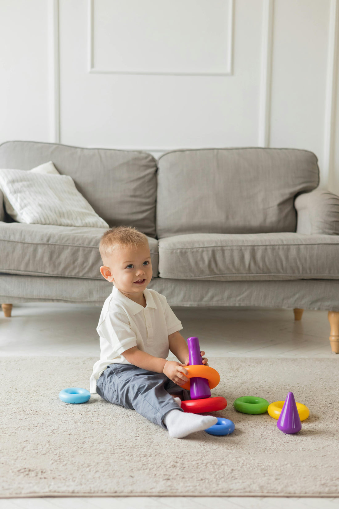 Toddler boy playing with stacking toy in front of couch